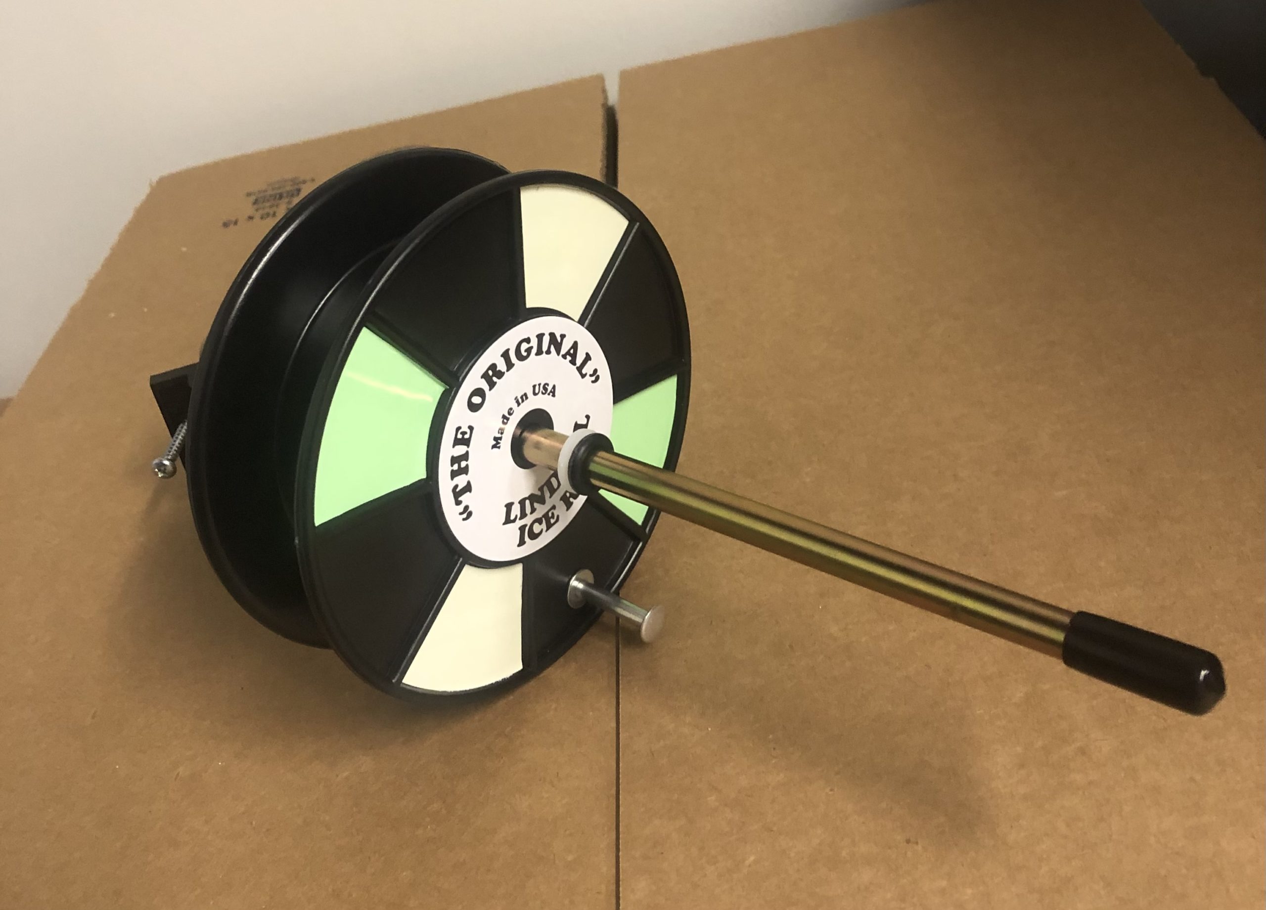 A Lindell Ice Rig Rattle Reel sitting on top of a cardboard box.