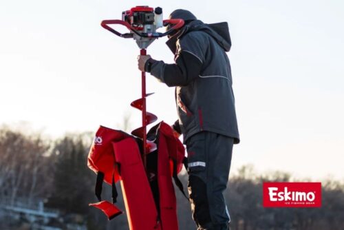 A man in a red jacket is holding an Eskimo Stingray 33cc 2-Cycle Viper® Engine Ice Auger.