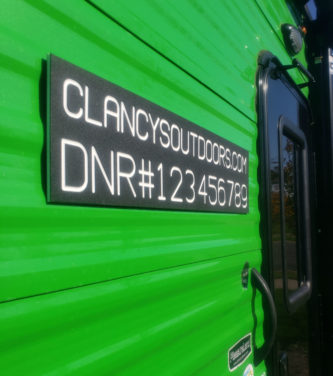 A green RV with a sign that says Custom DNR License Sign for Fish House.