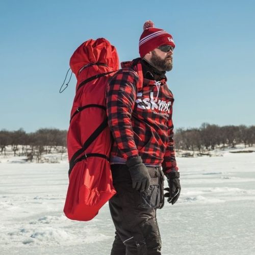 A man carrying an Eskimo Fatfish 949i HUB Ice Shelter on his back.