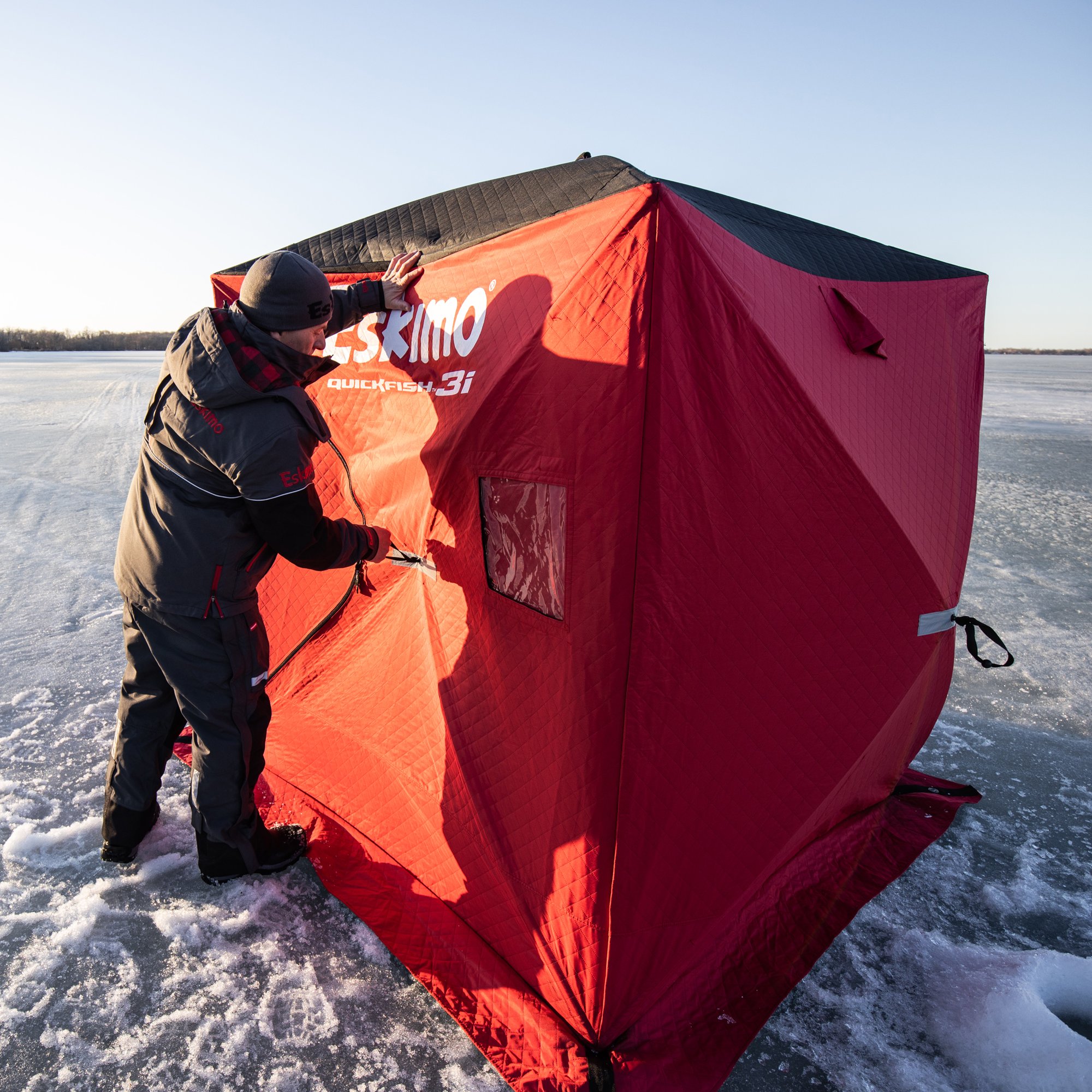 A man setting up the Eskimo 69445 Quickfish 3i Portable Insulated Pop-Up Ice Fishing Shelter, 3 Person on the ice.