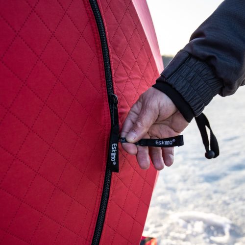 A person is holding a Eskimo 69445 Quickfish 3i Portable Insulated Pop-Up Ice Fishing Shelter, 3 Person with a zipper on it.
