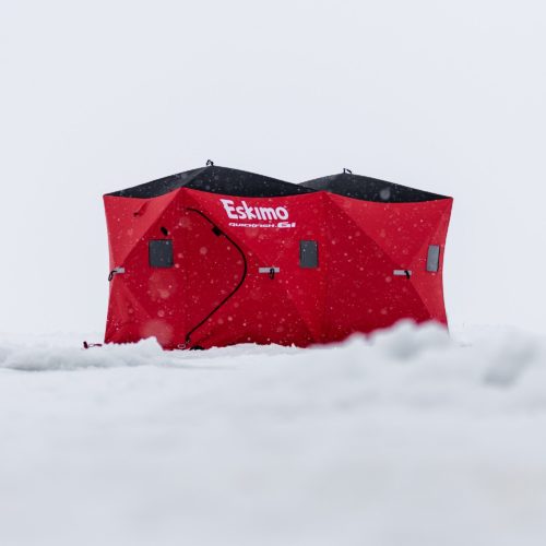 A Eskimo 36150 QuickFish 6i Pop-Up Portable Insulated Ice Fishing Shelter, 6 Person sits on top of a pile of snow.