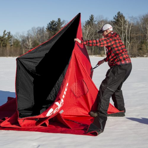 A man is holding a Eskimo 36150 QuickFish 6i Pop-Up Portable Insulated Ice Fishing Shelter, 6 Person in the snow.