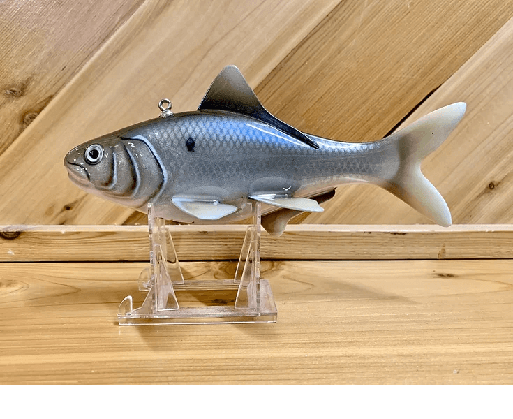 A gray plastic Gizzard Shad sitting on a wooden stand.