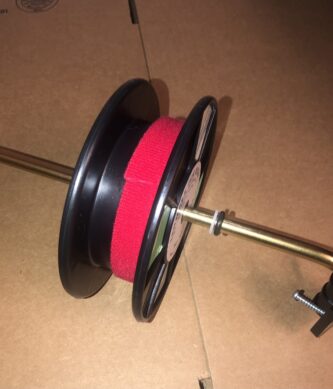 A red and black Line Keeper for Lindell Ice Rig or Other Rattle Reel on a cardboard box.