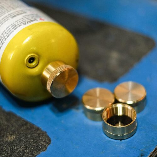 A set of Solid Brass Refill 1lb Propane Tank Caps with Seals next to a bottle of gas.