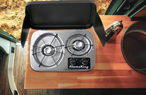 A Flame King 2 Burner Built-In RV Trailer Stove with Wind Shield sitting on top of a table in an rv.